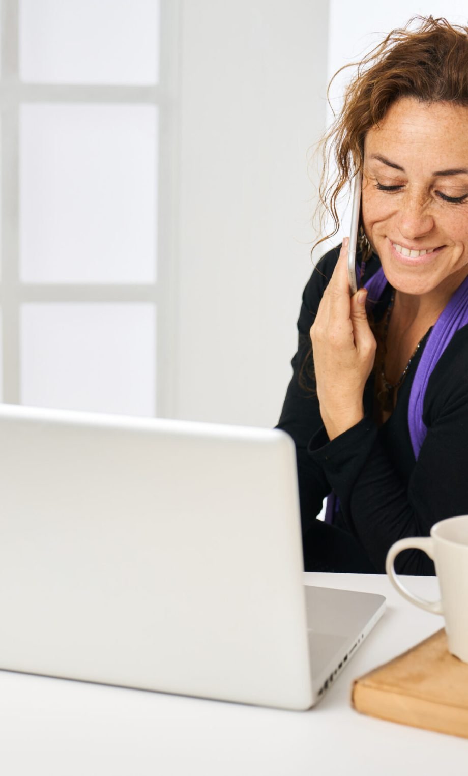 entrepreneurial woman working at her computer and answering a phone call with a cup of coffee